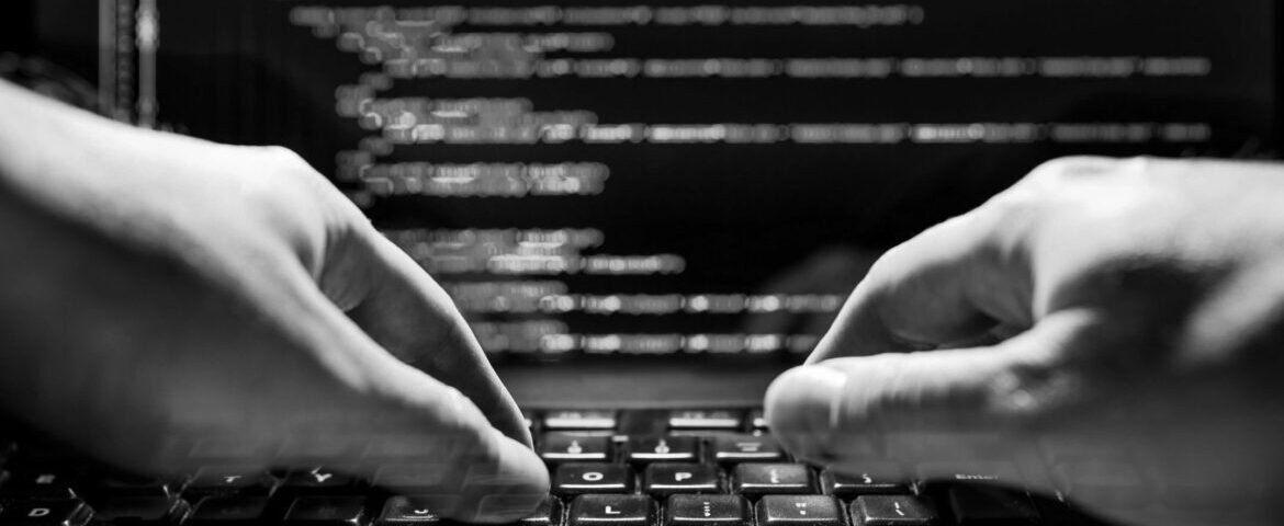 Close-up of hands typing on a keyboard with blurred code in the background.